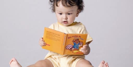 Bébé qui lit un livre assis par terre.